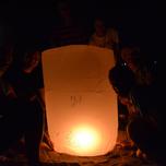 Group of people gathered around a lit sky lantern at night.